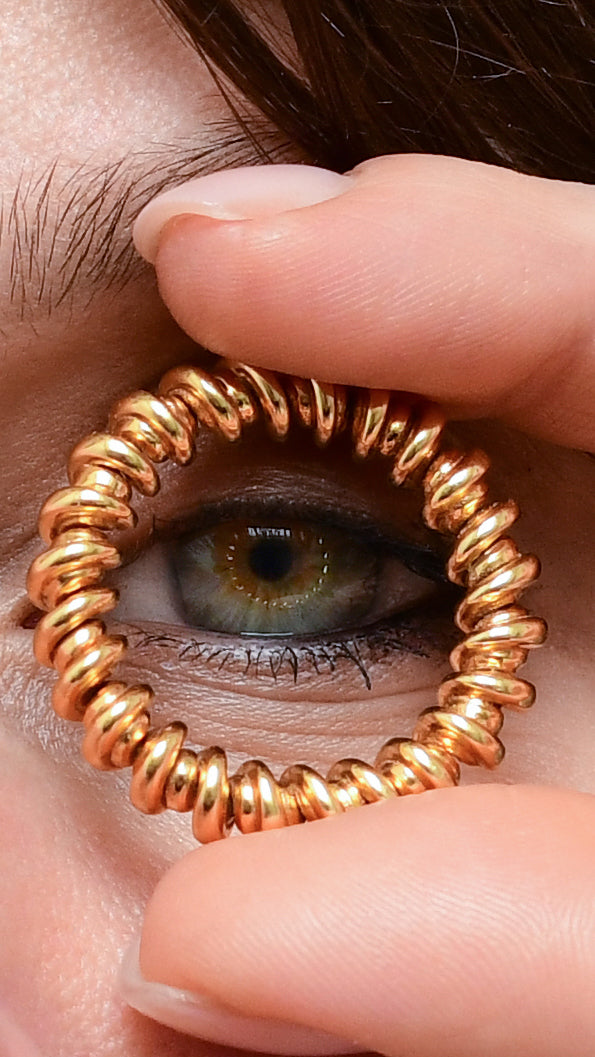 Gold spiral hair tie being worn around a finger with a close-up of an eye.
